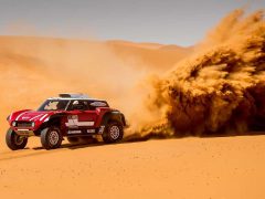 Een rode terreinwagen die door het zand rijdt tijdens de Dakar Rally.