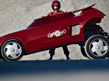 Een man in een rood pak staat naast een rode Sbarro-auto.