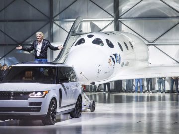 Een man die bovenop een Range Rover staat voor een ruimtevaartuig.