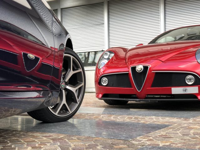 Twee Alfa Romeo Giulia Veloce-sportwagens geparkeerd voor een gebouw.