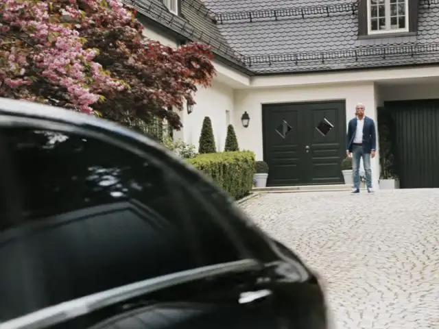 Een man, die lijkt op Dieter Zetsche, staat naast een auto voor een huis.