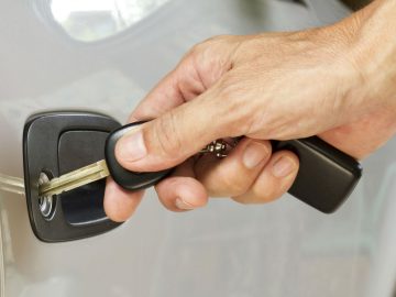 Een persoon die de deur van een auto opent met een autosleutel.