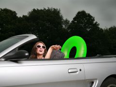 Een vrouw bestuurt een cabrio met een groene ring op de achterbank.