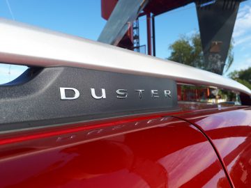 Een close-up van het Dacia Duster TCe 130-logo op een rode auto.