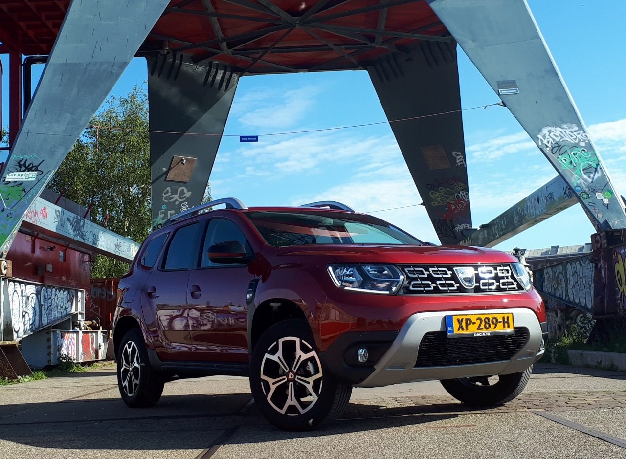 Een rode Dacia Duster TCe 130 SUV geparkeerd voor een brug.