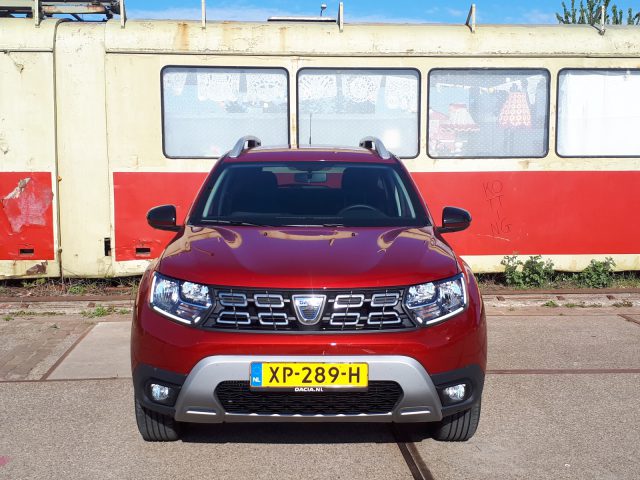 Een rode Dacia Duster TCe 130 geparkeerd voor een trein.