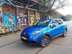 Een blauwe Fiat 500X Opening Edition geparkeerd voor een met graffiti bedekt gebouw.