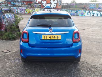 Een blauwe Fiat 500X Opening Edition geparkeerd voor een met graffiti bedekte muur.