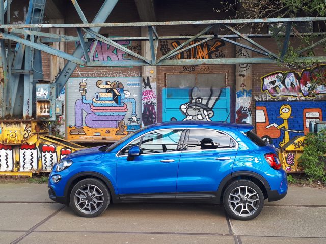 Een blauwe Fiat 500X Opening Edition geparkeerd voor een met graffiti bedekt gebouw.