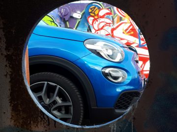 Een blauwe Fiat 500X Opening Edition weerspiegelt zich in een gat in de muur.