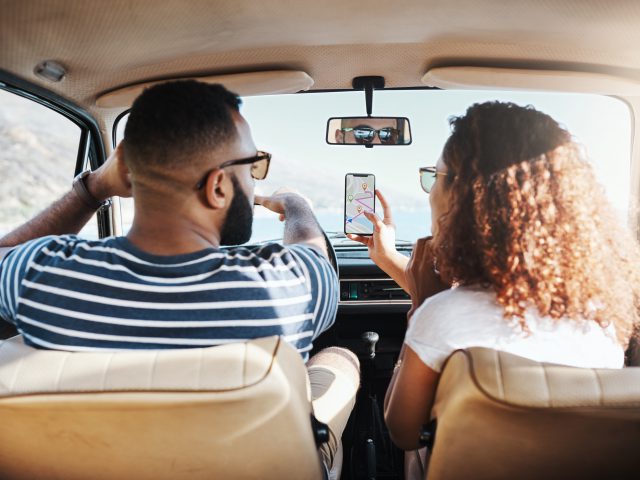 Twee mensen zitten op de achterbank van een auto en kijken naar een app op hun telefoon.