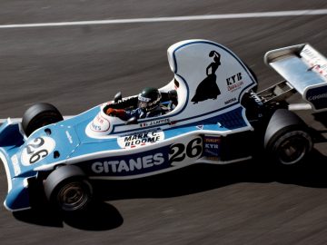 Een blauw-witte Ligier-raceauto die op een circuit rijdt.