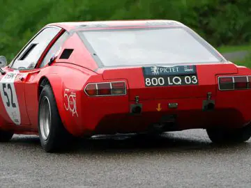 Een rode Ligier-sportwagen die op een natte weg rijdt.