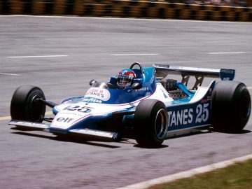 Een man rijdt in een blauwe Ligier-raceauto op een circuit.
