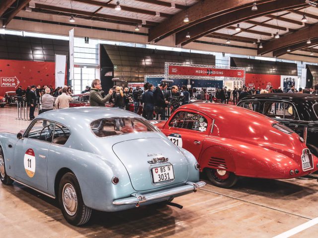 Een groep klassieke auto's geparkeerd in een grote ruimte voor de Mille Miglia 2019.