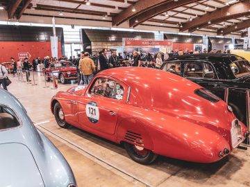 Een groep mensen kijkt in een garage naar oude auto's en haalt herinneringen op aan de Mille Miglia 2019.