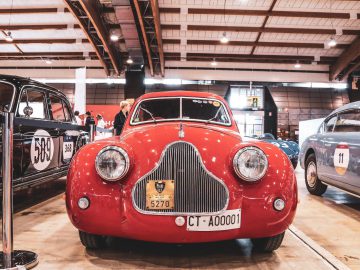 In een gebouw staat een oude rode auto van de Mille Miglia 2019 tentoongesteld.