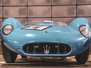 Een blauwe vintage raceauto van de Mille Miglia 2019 staat geparkeerd in een garage.