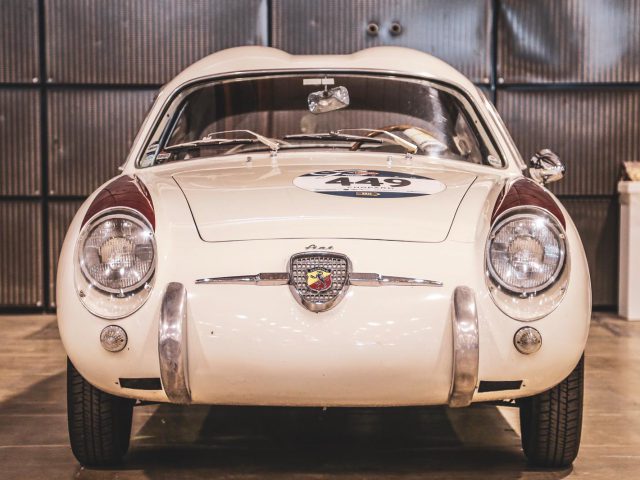 Een witte vintage auto, deelnemer aan de Mille Miglia 2019, staat geparkeerd in een garage.