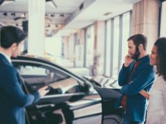 Een man en een vrouw die zichtbaar gestresseerd naar een auto in de showroom kijken.