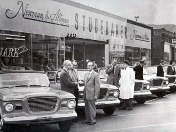 Een groep mannen staat voor een autodealer Studebaker Avanti.