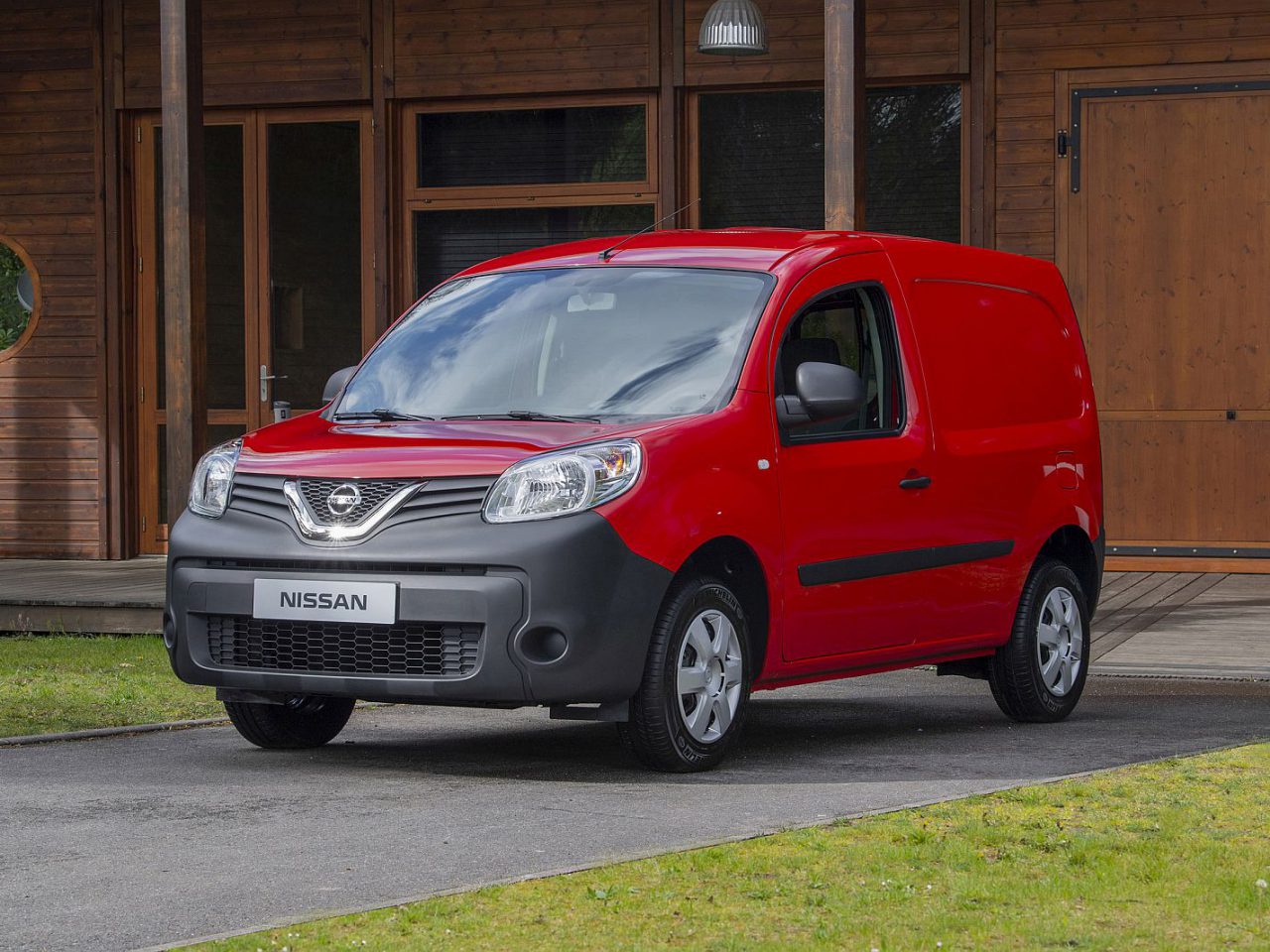 Een rood Nissan NV250-busje geparkeerd voor een huis.