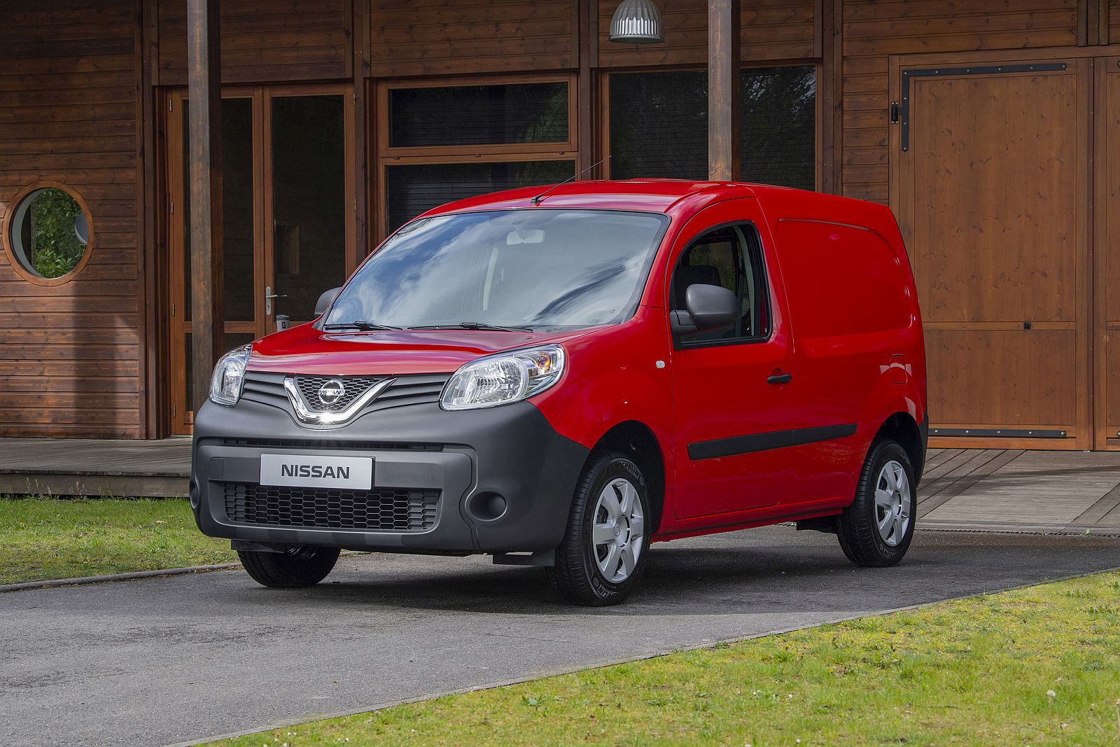 Een rood Nissan NV250-busje geparkeerd voor een huis.