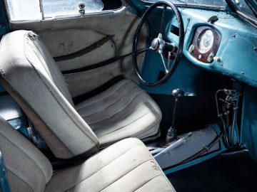 Het interieur van een oude Porsche Type 64 met blauwe stoelen en stuurwiel.