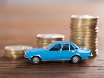 Op stapels autoverzekeringsmunten staat een blauwe speelgoedauto.