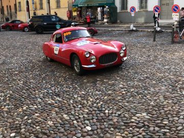 Een rode vintage auto van de Mille Miglia 2019 staat geparkeerd op een geplaveide straat.