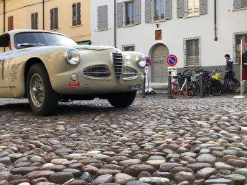 Een klassieke auto uit Mille Miglia 2019 staat geparkeerd op een geplaveide straat.