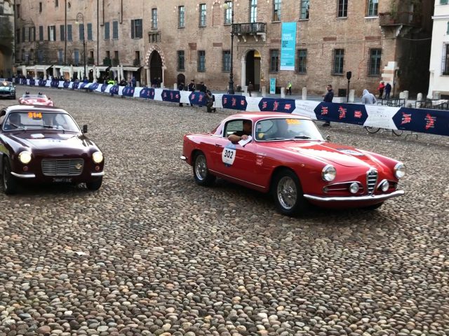 Twee klassieke auto's van de Mille Miglia 2019 staan geparkeerd op een geplaveide straat.
