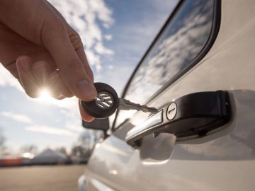 Een persoon opent de deur van een auto met een autosleutel.