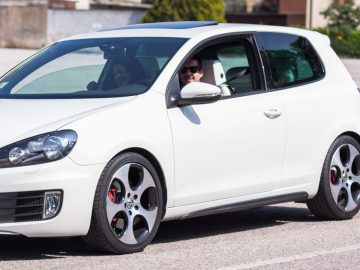 Een witte Volkswagen Golf GTI, gedekt door een autoverzekering, rijdt door de straat.