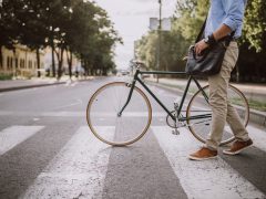 Een man die een straat oversteekt met een fiets met autoreclame.