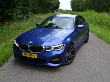 De blauwe BMW 3 Serie sedan rijdt over een landweg.