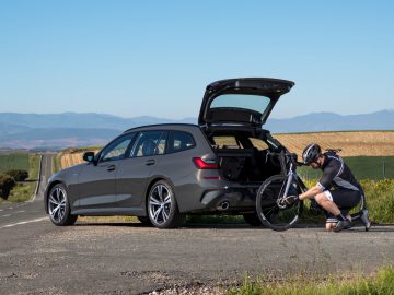 Een man zet zijn fiets in de kofferbak van een BMW.