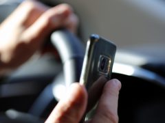 Een persoon die een mobiele telefoon vasthoudt terwijl hij autorijdt, riskeert een boete.