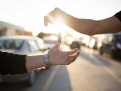 Een man die op een parkeerplaats een autosleutel aan iemand anders overhandigt als onderdeel van een MaaS-overeenkomst (Mobility as a Service).