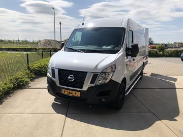 Een witte Nissan NV400-bestelwagen geparkeerd voor een hek.