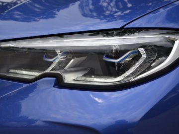 De koplamp van een blauwe BMW 3 Serie.