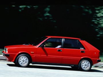 Er rijdt een rode Lancia Delta over de weg.