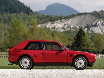 Een rode Lancia Delta geparkeerd voor een berg.
