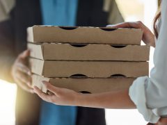 Een vrouw houdt een stapel Nieuw-pizzadozen vast.