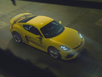 Een gele Porsche 718 Cayman die 's nachts door een straat rijdt.