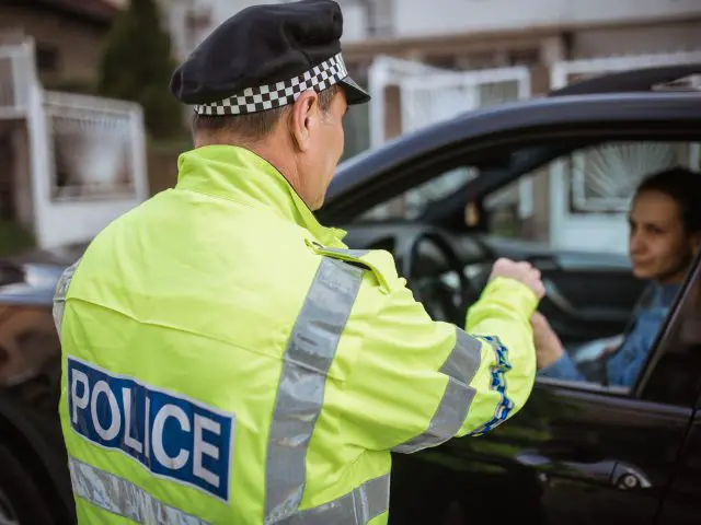 Een politieagent geeft een vrouw een ritje in een auto om haar voor te lichten over verkeersveiligheid.