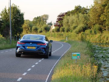 Een blauwe BMW rijdt over een weg vlakbij een vijver.