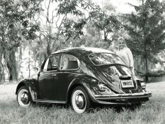 Een zwart-witfoto van een vrouw die naast een Volkswagen Kever staat.