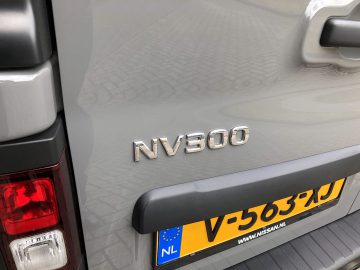 De achterkant van een zilverkleurige Nissan NV300 met een kentekenplaat erop.