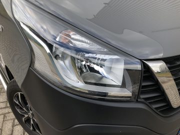 Een close-up van de koplamp van een zwarte bestelwagen van Nissan NV300.